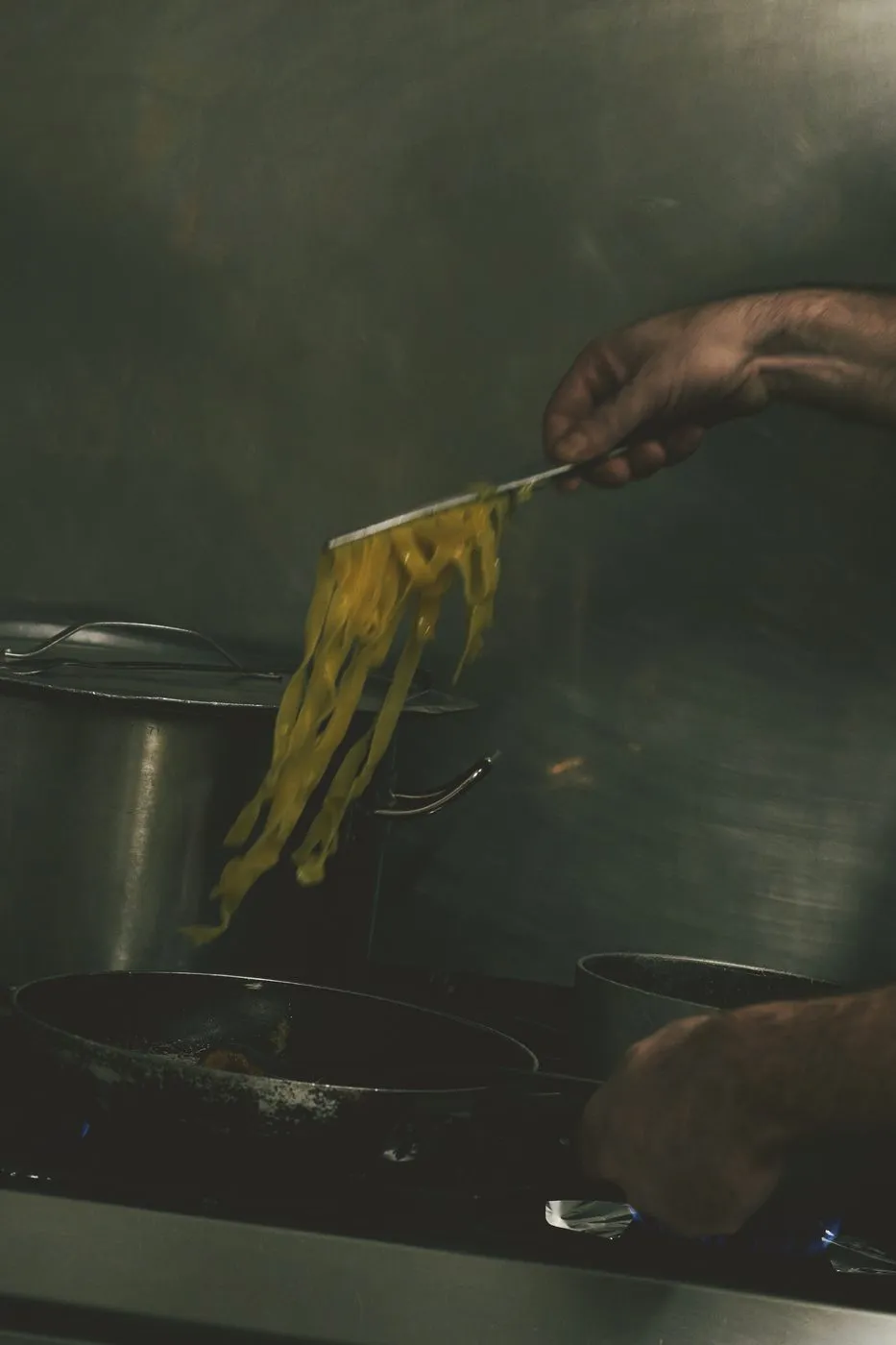 Pasta fresca sollevata dalla pentola nella cucina in penombra